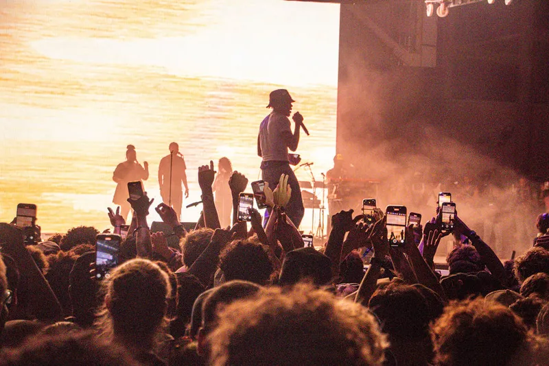 Performers and raised phones silhouetted against a sunset-lit stage