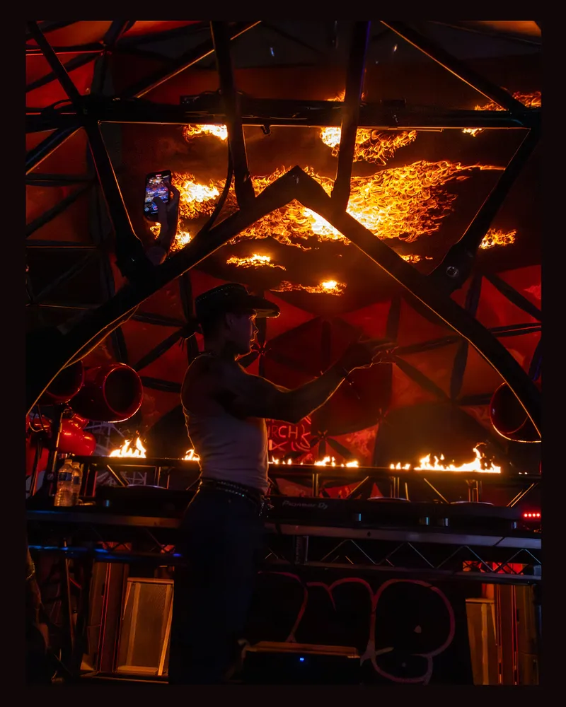Performer under geometric stage trusses and orange pyrotechnics